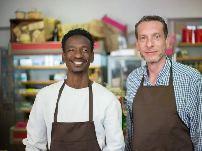 Two local shop owners in aprons behind the counter of their store